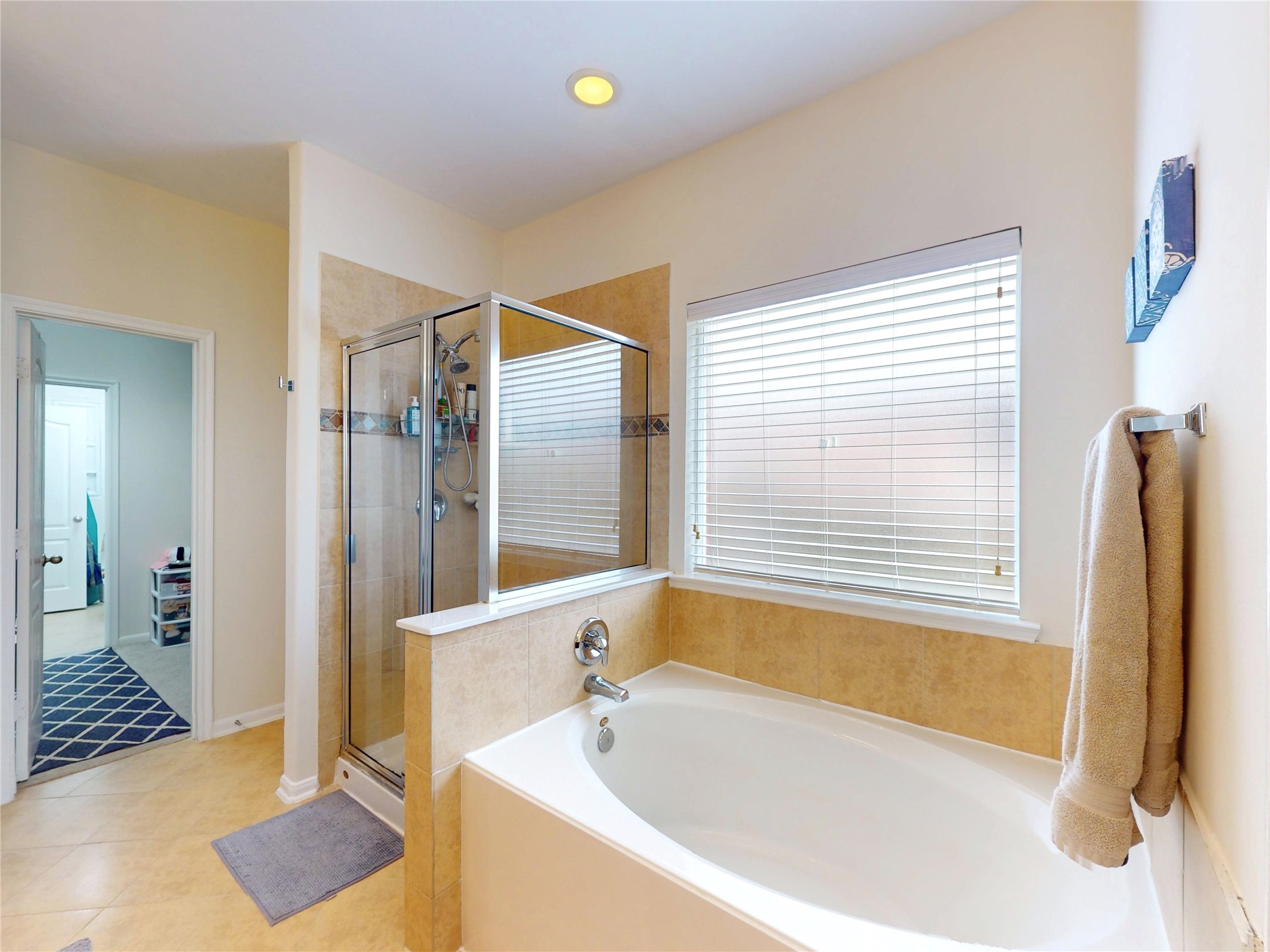 17402 Rainer Valley Lane Humble, TX 77346 - Photo 18 of 33 This bathroom features a spacious soaking tub and a separate glass-enclosed shower. It has light tiles, a window with blinds for natural light, and a towel rack, creating a bright and inviting space.