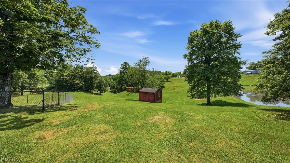 89 Dagg Road Parkersburg, WV 26101 - Photo 9 of 45 Expansive green space featuring a red shed, mature trees, a fenced area, and a visible pond in the distance