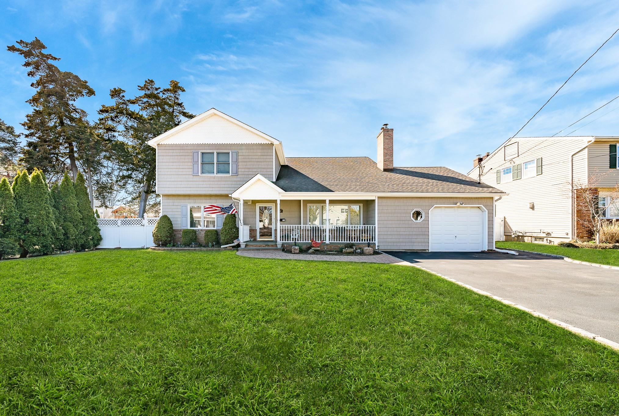 55 Sunset Road Massapequa, NY 11758 - Photo 1 of 1 View of front facade with concrete driveway, fence, an attached garage, a front lawn, and covered porch