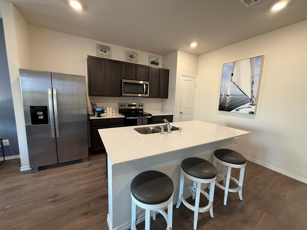 317 Clematis Street Princeton, TX 75407 - Photo 13 of 38 Kitchen with appliances with stainless steel finishes, dark wood-style floors, a kitchen island with sink, a breakfast bar area, and light stone counters