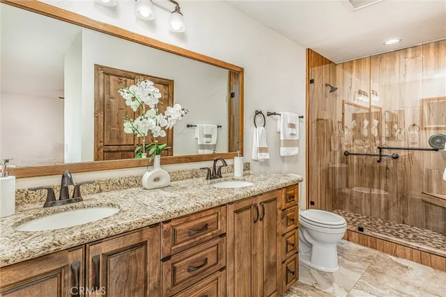 a bathroom with a granite countertop sink a toilet a mirror and shower