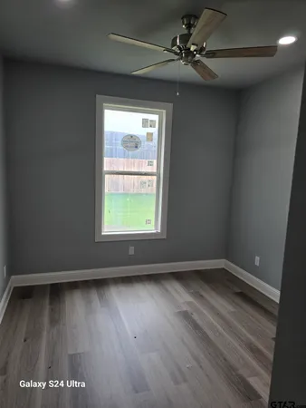 an empty room with wooden floor fan and windows