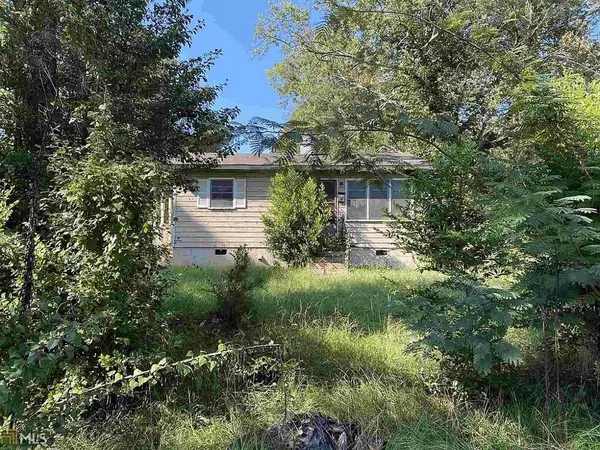 a view of a house in front of a yard with plants and large trees