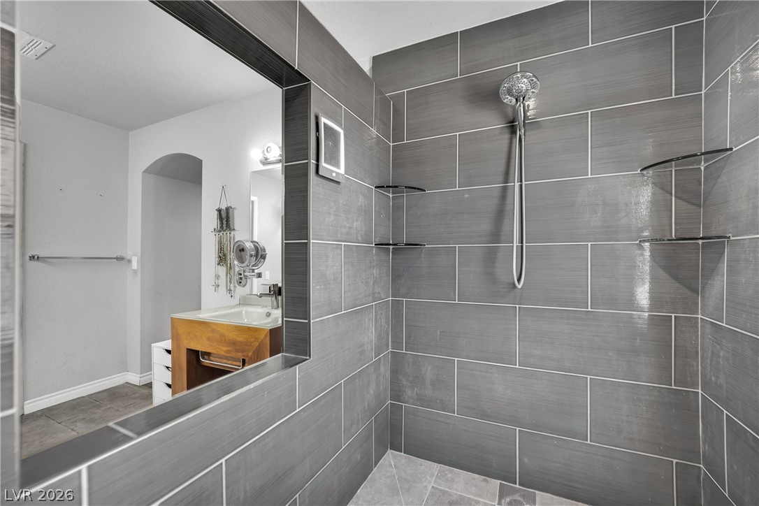420 North Racetrack Road Henderson, NV 89015 - Photo 10 of 52 A sleek, tiled shower with integrated shelving and modern fixtures, featuring a large mirror reflecting a vanity area.
