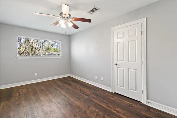 an empty room with wooden floor chandelier fan and windows