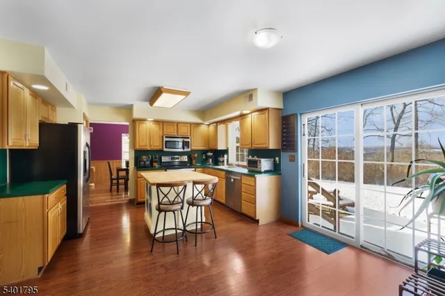 a kitchen with stainless steel appliances kitchen island granite countertop a refrigerator a stove a microwave oven a dining table and chairs with wooden floor