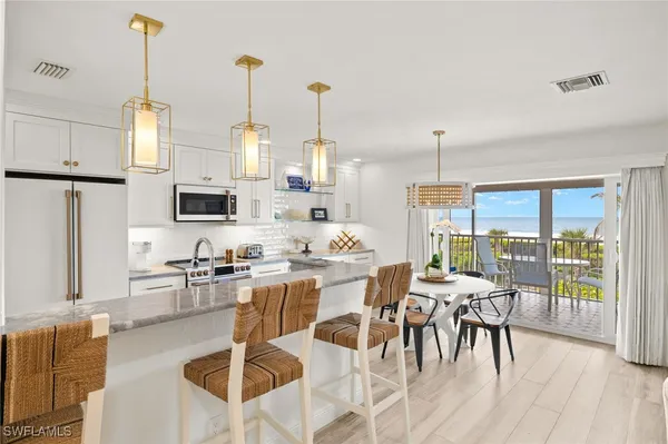 a kitchen with stainless steel appliances kitchen island granite countertop a stove a refrigerator a dining table and chairs with wooden floor