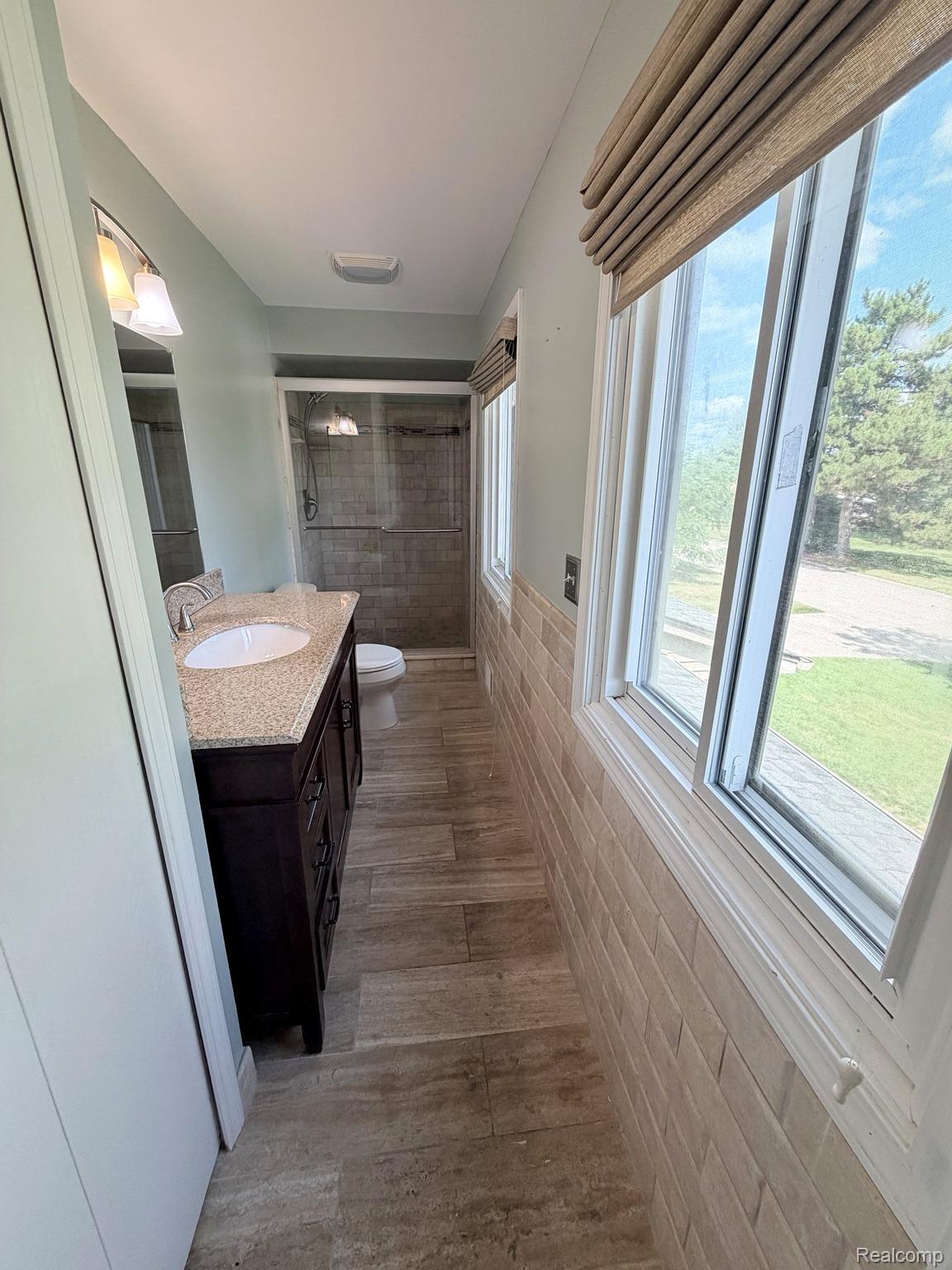 2070 Winchester Road Rochester, MI 48307 - Photo 28 of 34 Primary bathroom featuring a wood-finish vanity with quartz countertop and rectangular vessel sink, large-format tile shower enclosure, and abundant natural light from expansive multi-pane windows overlooking landscaped grounds