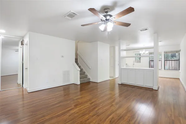 a view of an empty room with wooden floor and a kitchen
