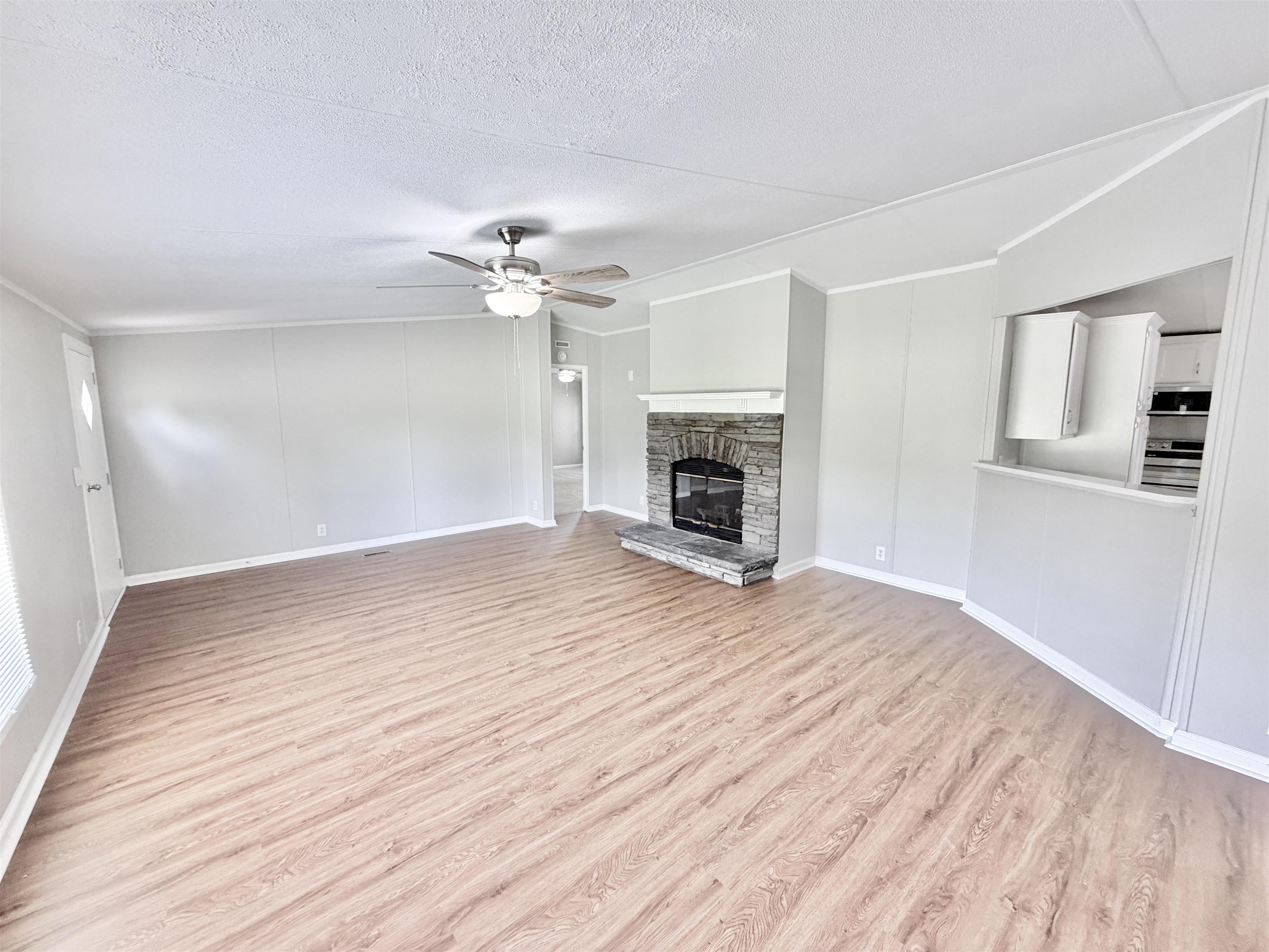 1655 Fayne Road Brighton, TN 38011 - Photo 4 of 28 Spacious living area featuring wood-finish flooring, a stone-surround fireplace with hearth, and a ceiling fan with integrated lighting