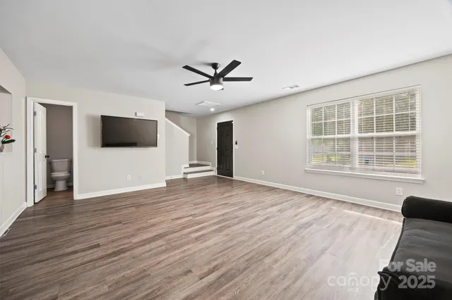 a view of a livingroom with a flat screen tv ceiling fan and wooden floor