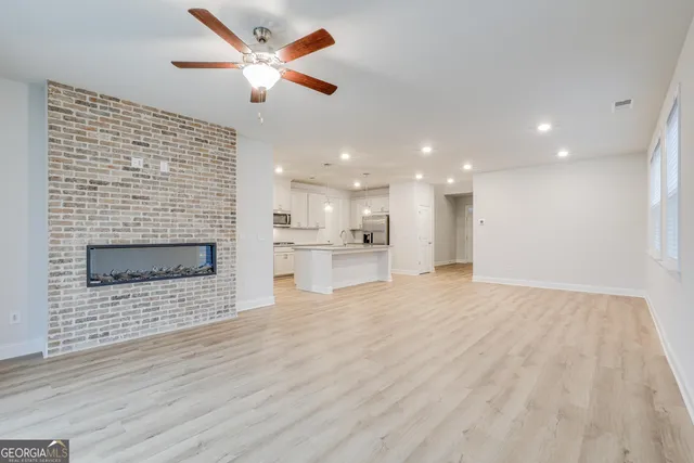a view of an empty room and kitchen with fireplace ceiling fan