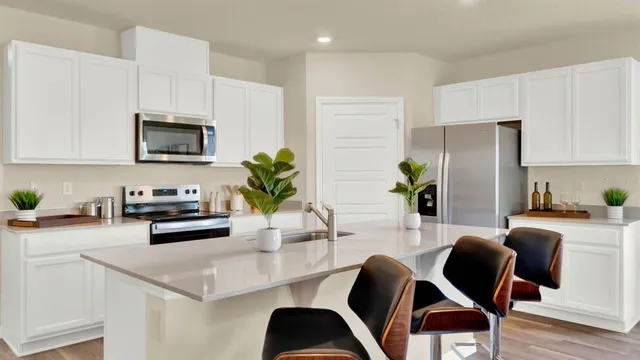 a kitchen with stainless steel appliances kitchen island granite countertop a refrigerator a stove a sink dishwasher and white cabinets with wooden floor