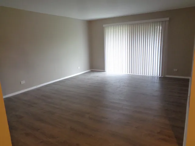 an empty room with wooden floor and windows with curtains