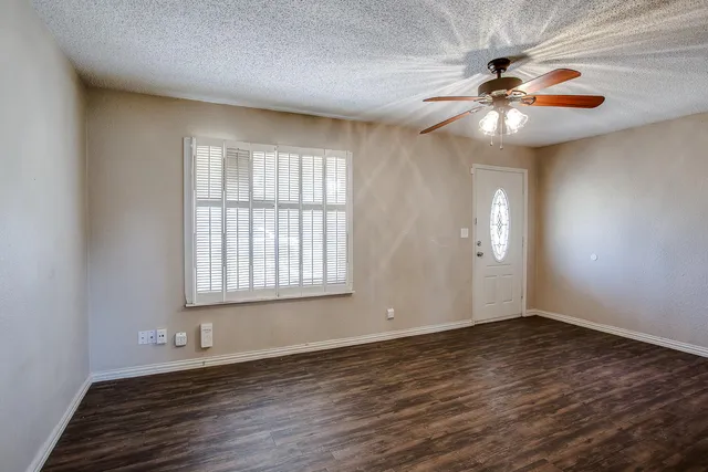 an empty room with wooden floor fan and windows