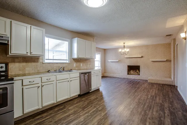 a large kitchen with granite countertop a stove top oven a sink dishwasher and a fireplace with wooden floor