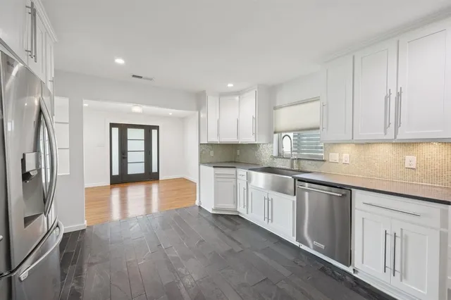 a large kitchen with stainless steel appliances a refrigerator a sink dishwasher a oven and a dining table with wooden floor