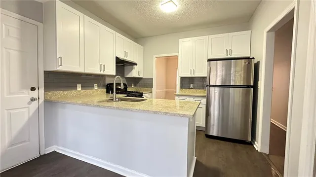 a kitchen with stainless steel appliances granite countertop a refrigerator a stove a sink and white cabinets with wooden floor