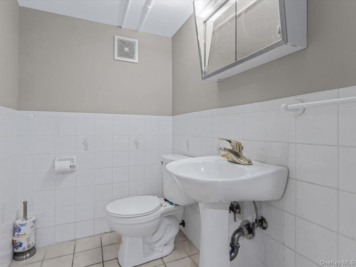 217-32 Corbett Road Queens, NY 11361 - Photo 22 of 25 Bathroom featuring tile walls, a wainscoted wall, and light tile patterned floors