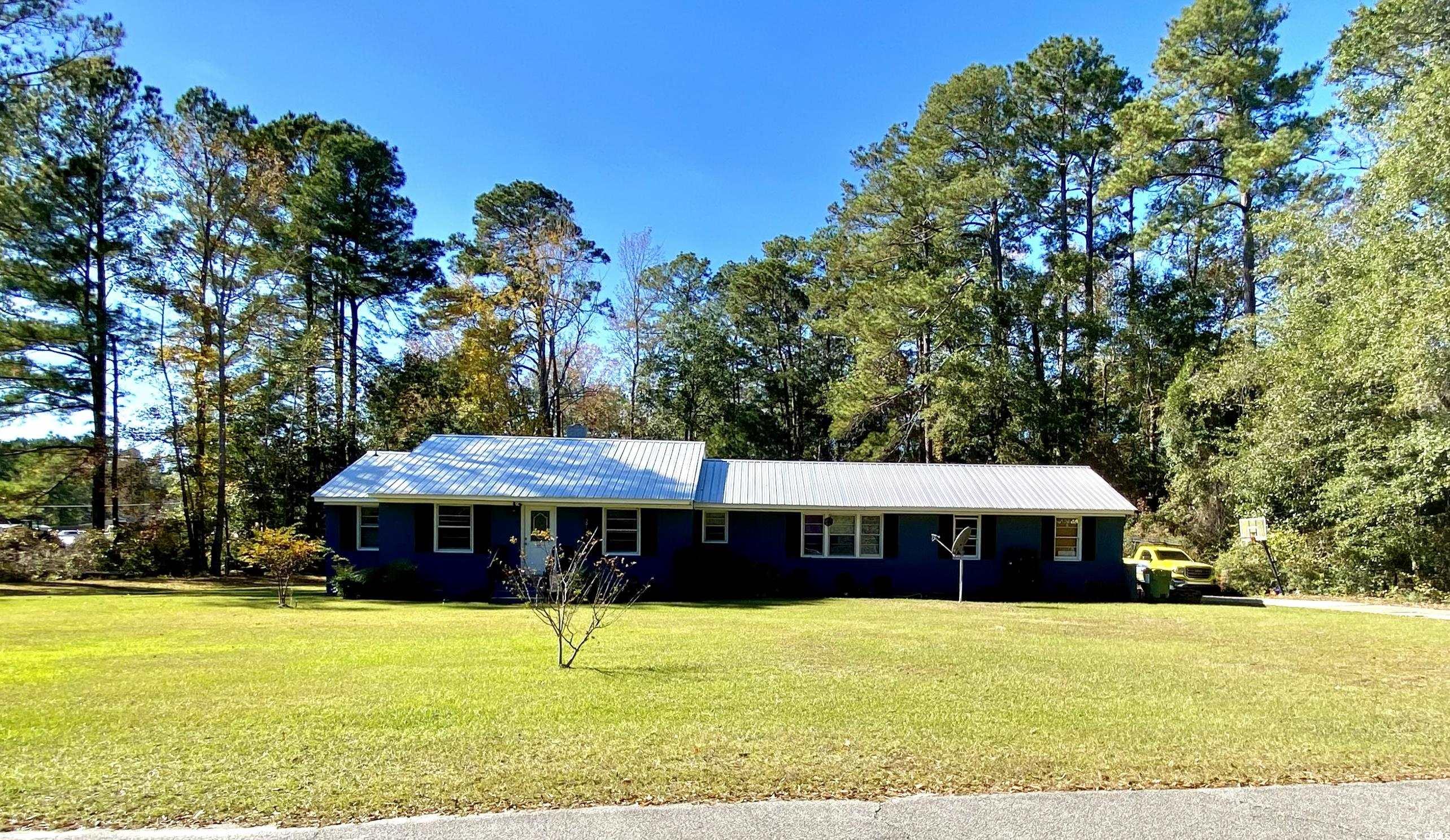 Single story home featuring a front lawn, a metal roof, and view of wooded area
