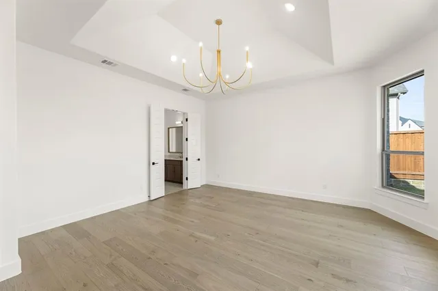 an empty room with wooden floor chandelier and windows