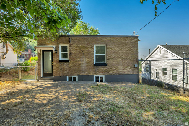 662 29th Street Ogden, UT 84403 - Photo 22 of 23 Brick exterior featuring a rear entry door with an awning, multiple windows, and a partially fenced yard