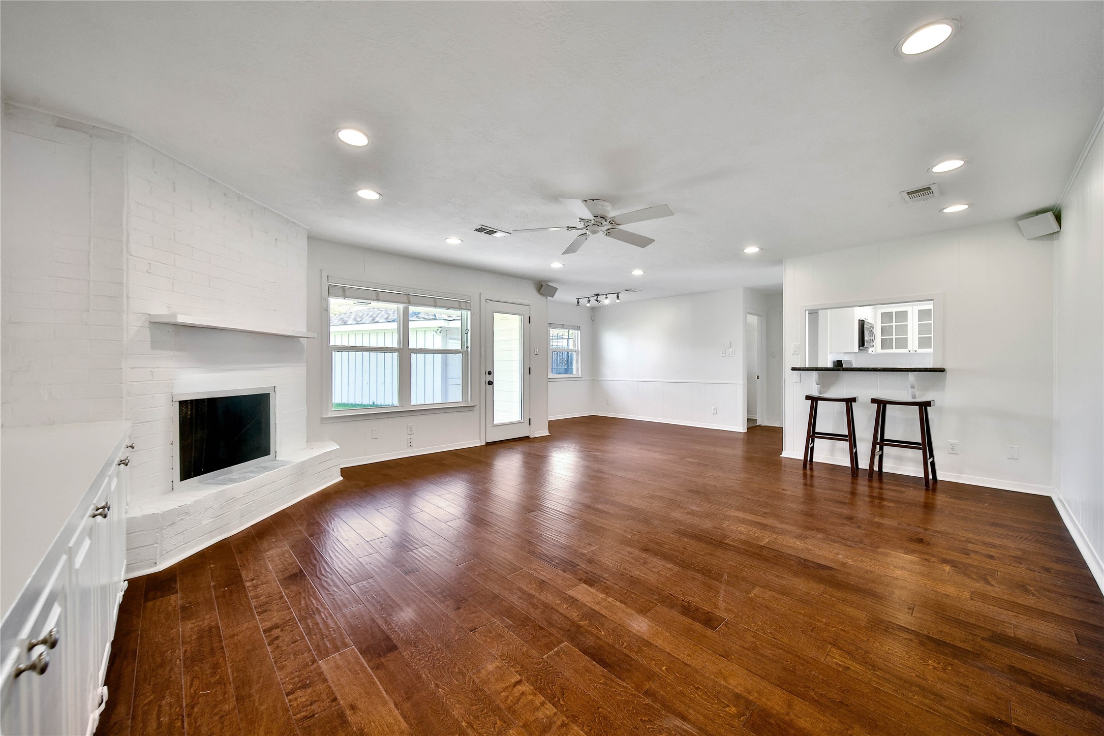 955 Thornton Road Houston, TX 77018 - Photo 7 of 27 Light-filled den with warm engineered wood floors, a white brick fireplace, and seamless flow into the updated kitchen via a granite pass-through bar. The kitchen nook sits kitty-corner to the back right, creating a comfortable and functional dining space.