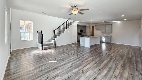 a view of an empty room and kitchen with wooden floor