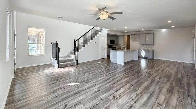 a view of an empty room and kitchen with wooden floor