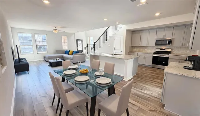 a open dining room with stainless steel appliances kitchen island granite countertop a dining table chairs and couches with wooden floor