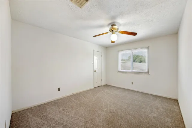 an empty room with chandelier fan and windows