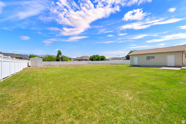 2467 South 2000 West Syracuse, UT 84075 - Photo 25 of 28 Expansive grassy yard area featuring a detached auxiliary building, a separate storage shed, and durable white vinyl fencing