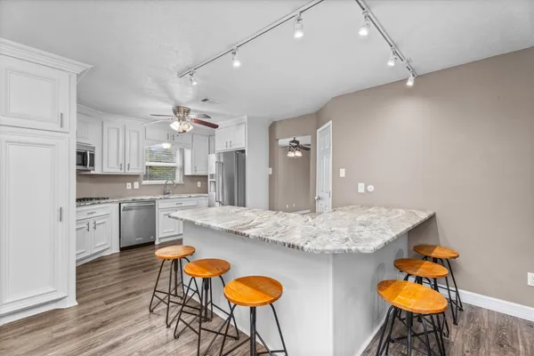 a kitchen with stainless steel appliances granite countertop a kitchen island a stove a sink dishwasher and white cabinets with wooden floor