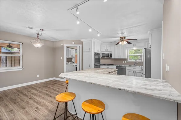 a large kitchen with granite countertop a stove a sink a dining table and chairs with wooden floor