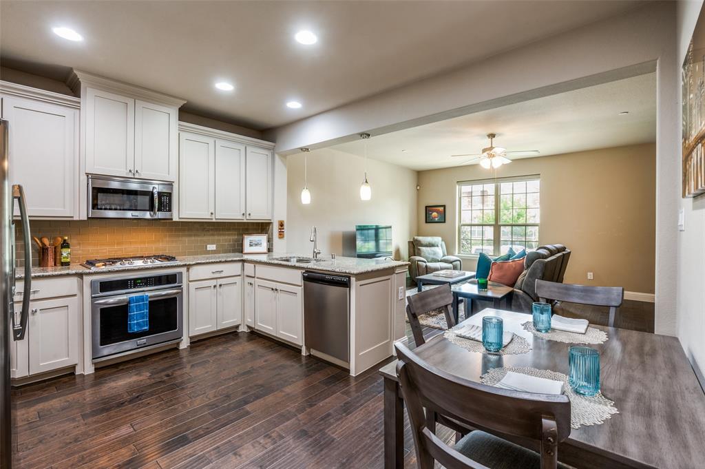 a open dining room with stainless steel appliances granite countertop a stove top oven a sink dishwasher a dining table and chairs with wooden floor