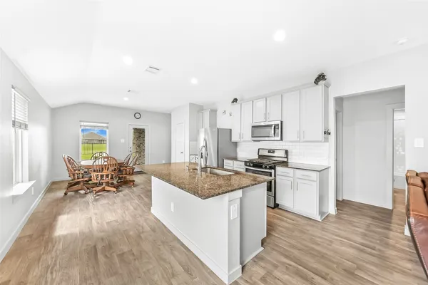 a living room with stainless steel appliances granite countertop wooden floor a kitchen island a stove a sink a refrigerator and cabinets