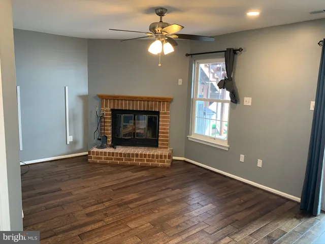 a view of an empty room with wooden floor fireplace and a window
