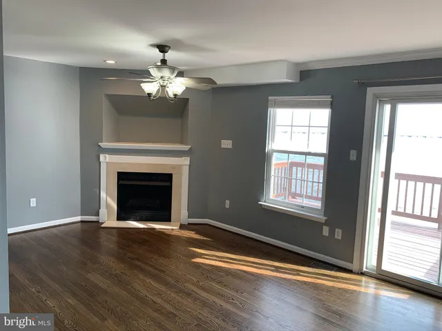 an empty room with wooden floor a chandelier fan and windows