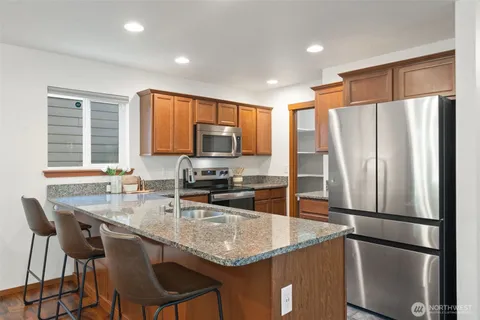 a kitchen with stainless steel appliances granite countertop a refrigerator a stove a sink a dining table and chairs