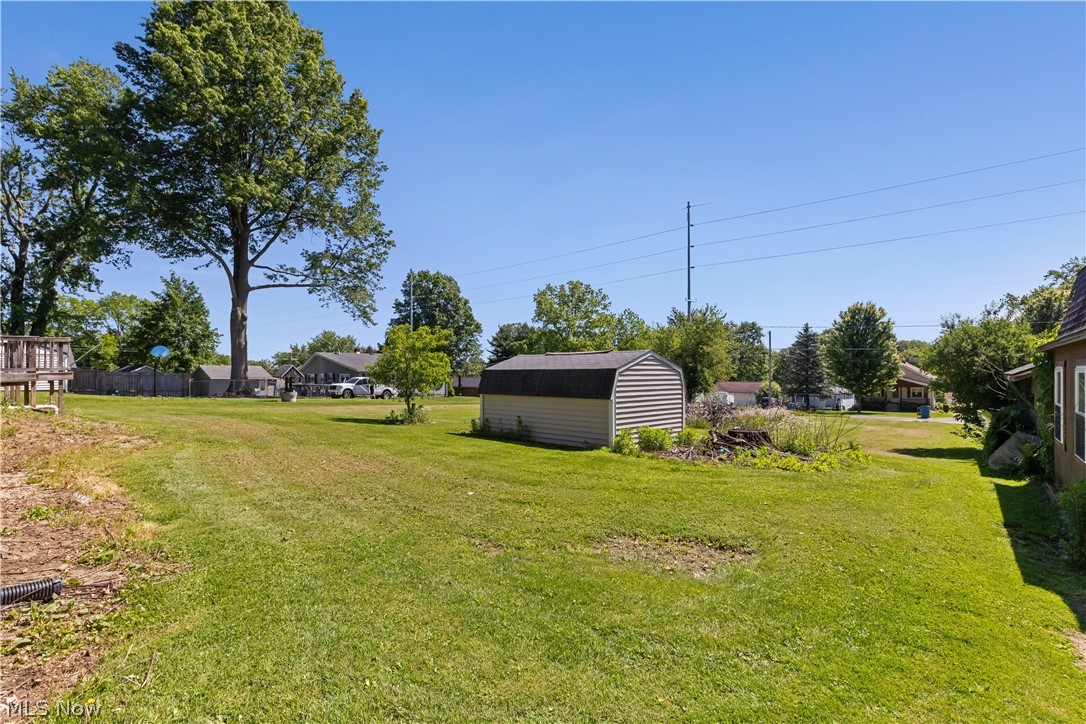 409 Edith Avenue Akron, OH 44312 - Photo 43 of 45 Expansive grassy yard featuring a wood-sided storage shed with a gambrel roof, a mature tree, and a partial wood deck