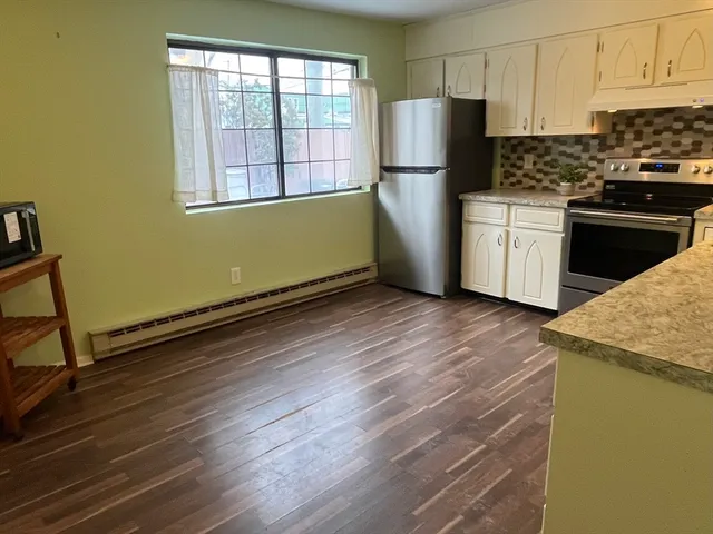 a kitchen with granite countertop a refrigerator a stove a sink and white cabinets with wooden floor