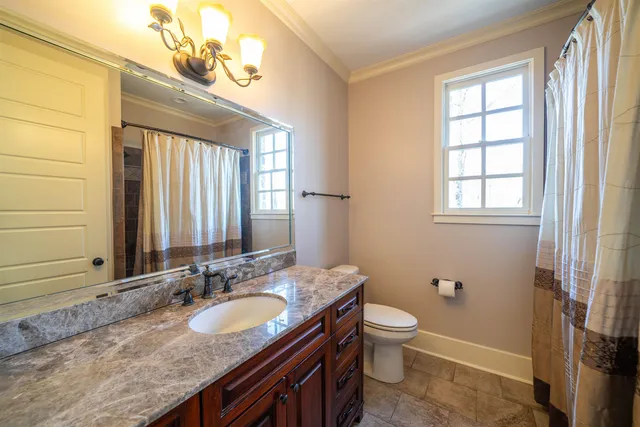 a bathroom with a granite countertop double vanity sink a mirror and a toilet