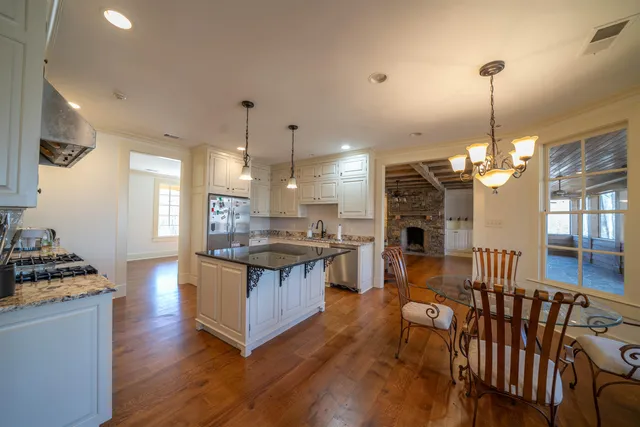 a open kitchen view with stainless steel appliances granite countertop a stove a refrigerator a oven a dining table and chairs with wooden floor