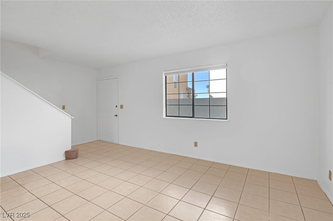 7030 Burcot Avenue, Unit F108 Las Vegas, NV 89156 - Photo 2 of 18 Spare room featuring light tile patterned floors, a textured ceiling, and stairway