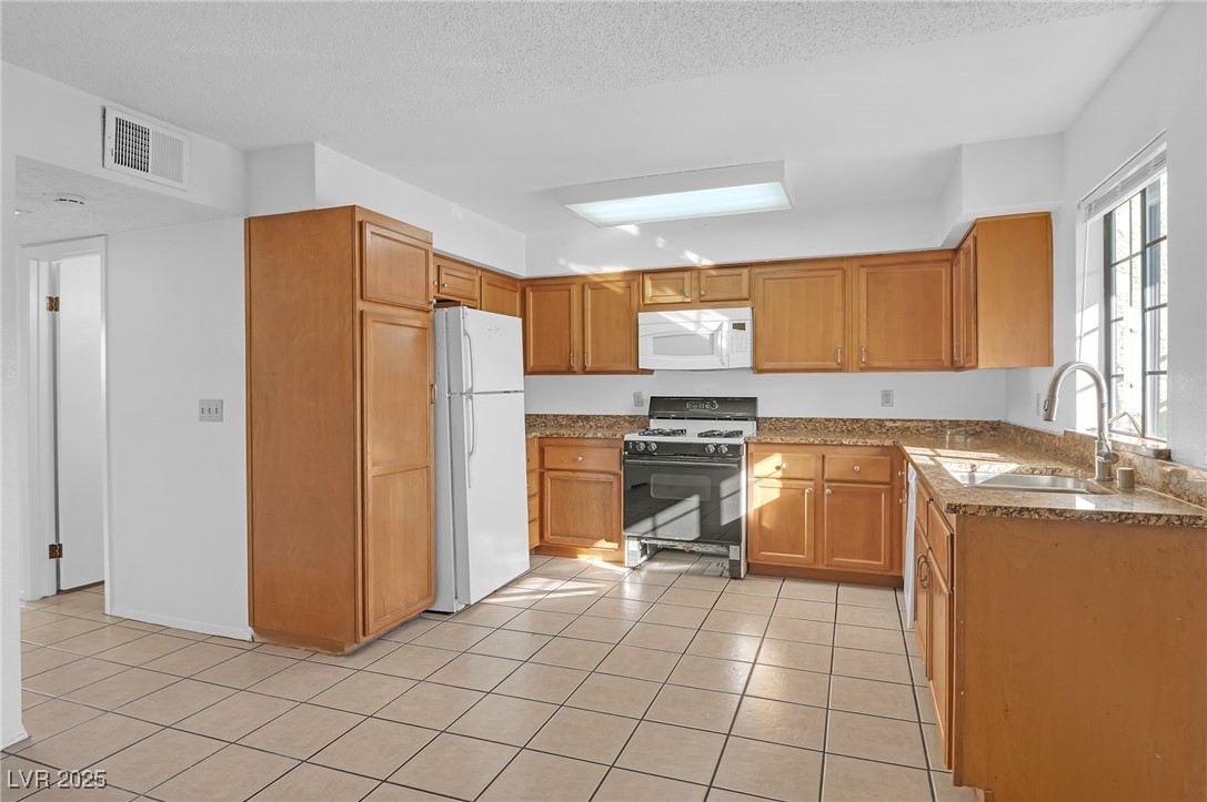 7030 Burcot Avenue, Unit F108 Las Vegas, NV 89156 - Photo 5 of 18 Kitchen with white appliances, light tile patterned floors, brown cabinets, dark stone counters, and a textured ceiling
