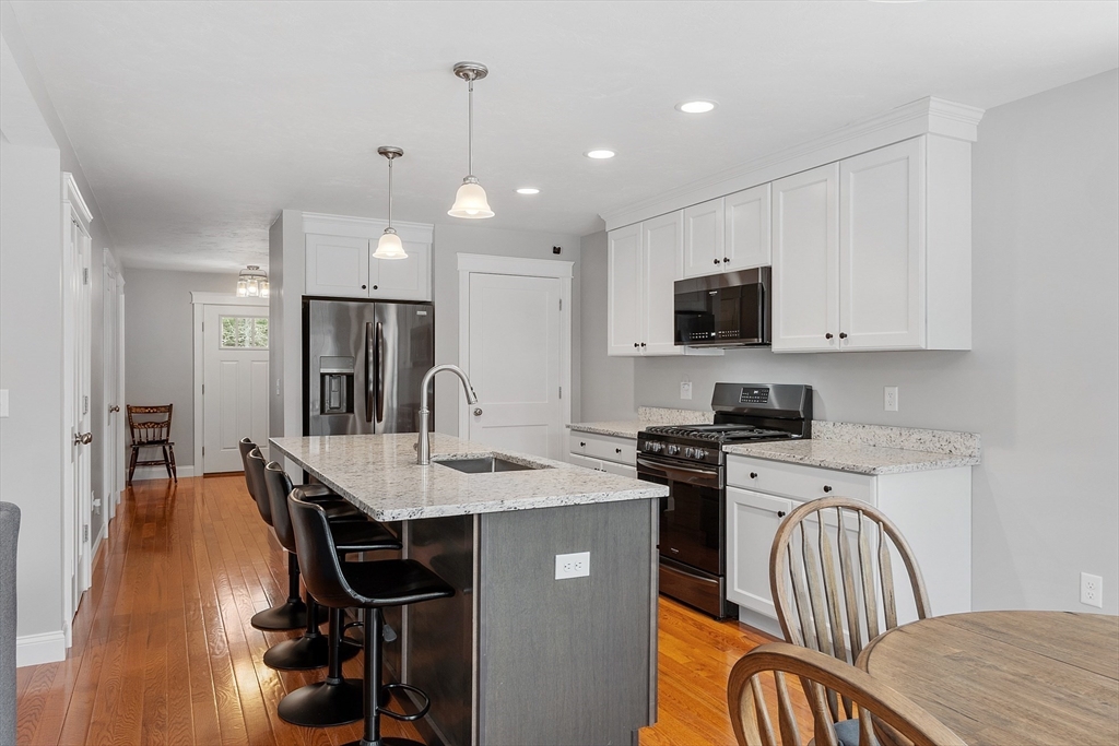 4 Scotch Pine Farm Way, Unit 1 Pepperell, MA 01463 - Photo 5 of 35 a kitchen with stainless steel appliances kitchen island granite countertop a stove a refrigerator a sink a dining table and chairs with wooden floor