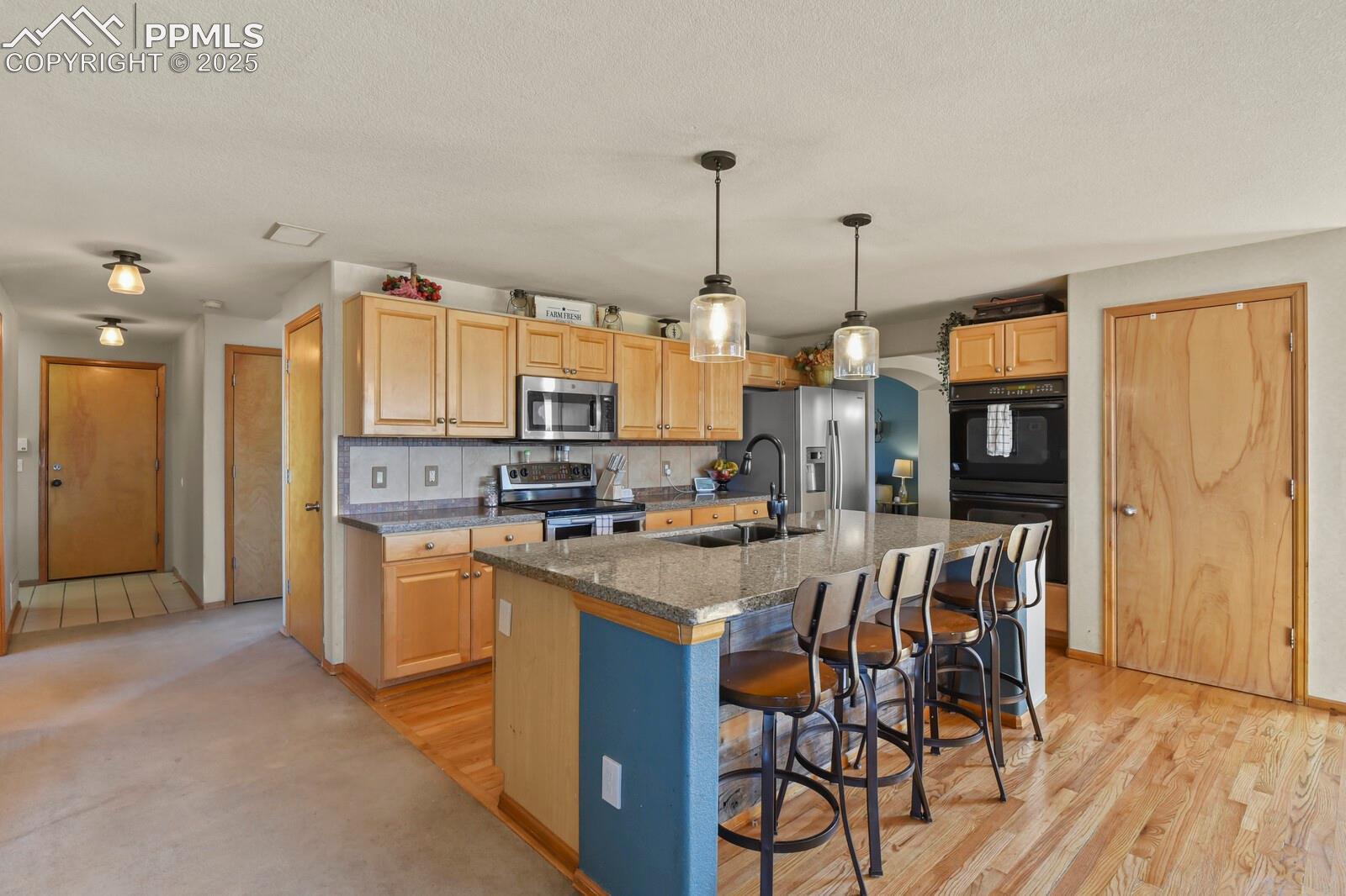 7660 Bullet Road Peyton, CO 80831 - Photo 12 of 50 Kitchen with stainless steel appliances, an island with sink, a breakfast bar, hanging light fixtures, and decorative backsplash