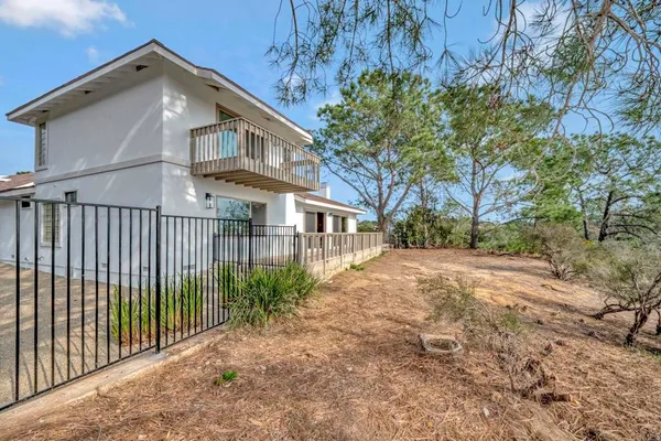 a view of a white house with large trees and wooden fence