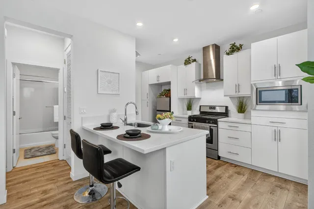 a kitchen with stainless steel appliances kitchen island granite countertop a stove a sink dishwasher a refrigerator white cabinets and wooden floor