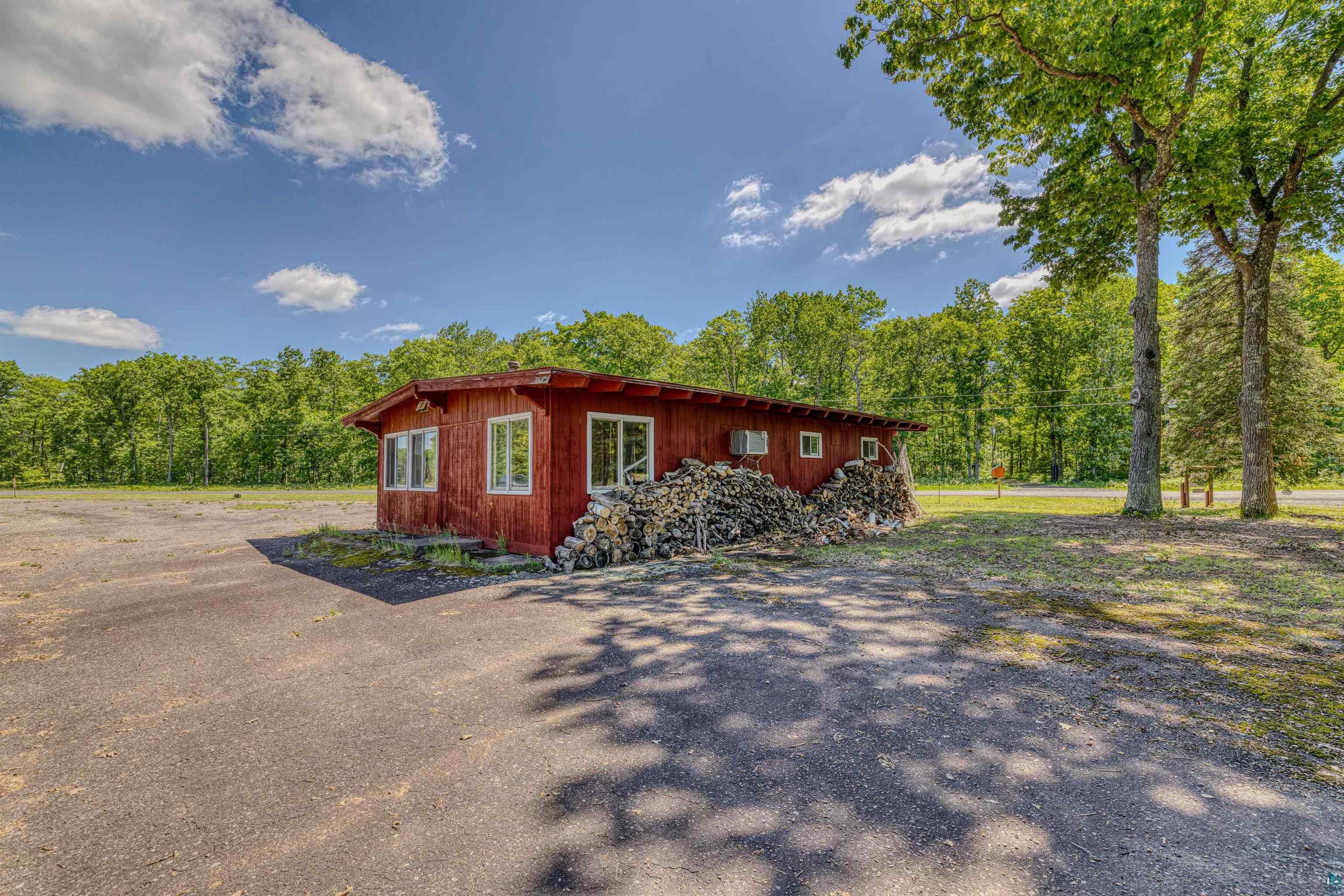 66075 Rooster Road Iron River, WI 54847 - Photo 48 of 52 Red-sided building with multiple windows, featuring a natural wood-colored roof and a stacked woodpile along one exterior wall